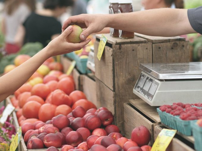 Banca de mercado com fruta, uma mão a entregar uma maçã a outra